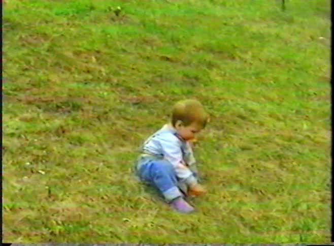 Charming vintage home video of a sweet toddler in overalls playing and walking on a grassy hill