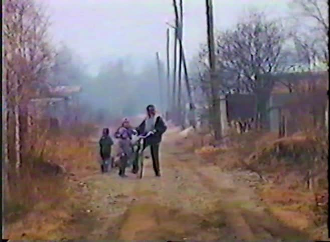 Vintage VHS footage shows a father and two children walking with a bicycle down a foggy rural road