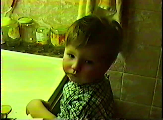 A cute toddler in a plaid shirt plays with running water in a bathroom sink in this vintage home movie