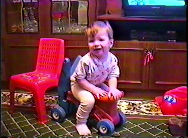 An adorable toddler on a ride-on toy plays with a slipper and then smiles happily