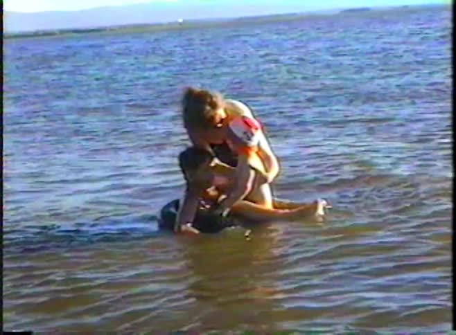A loving mother helps her two small children float and play on an inner tube in the shallow water of a lake