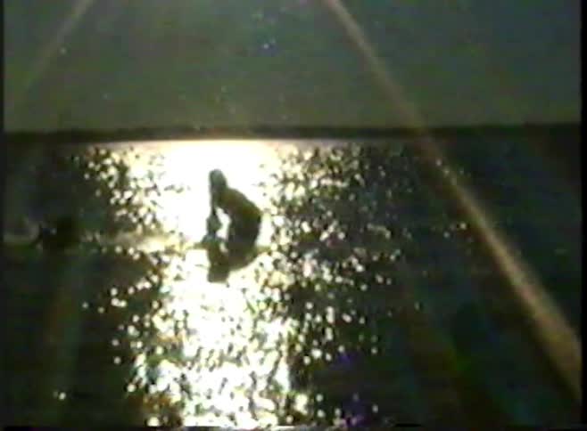 A grainy, vintage clip shows the silhouette of a mother and child playing in the shimmering water at sunset
