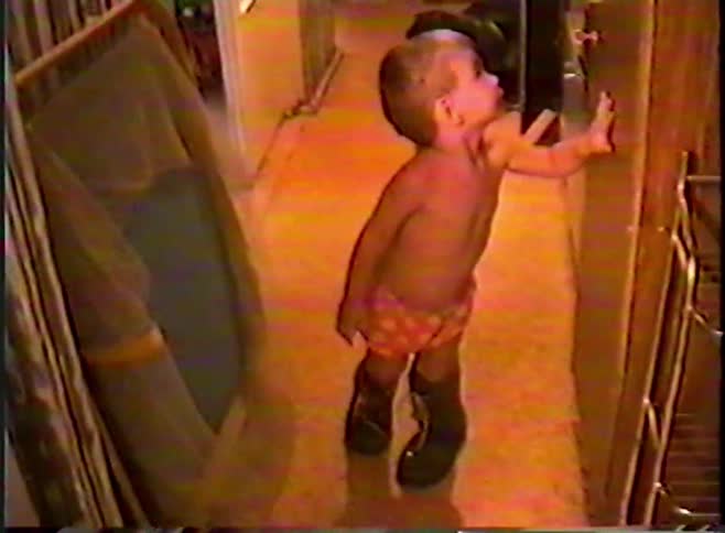 A cute toddler wearing only his underwear hilariously tries to walk around the house in a pair of oversized boots