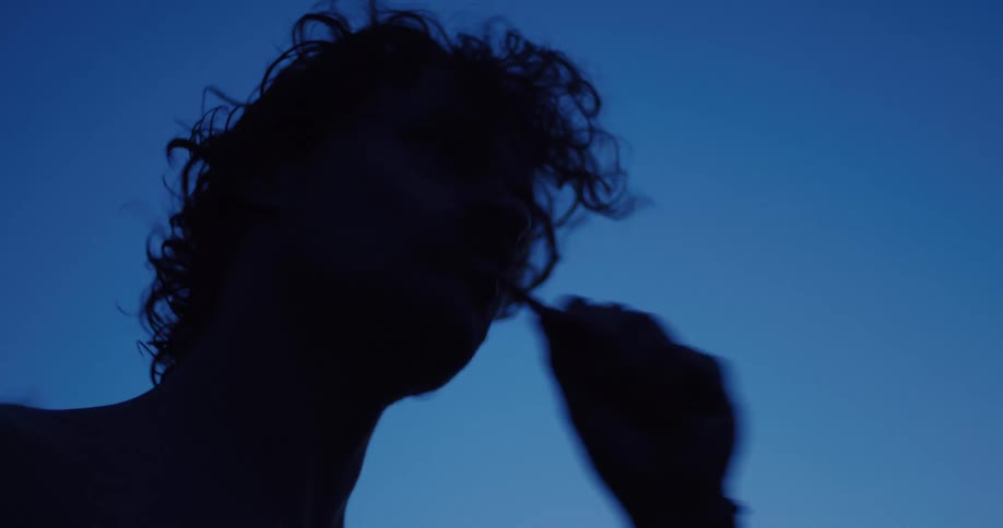Low angle silhouette of a person brushing their teeth against a dark blue sky at dusk