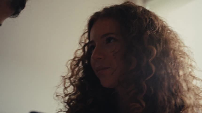 An intimate over-the-shoulder shot captures a young woman's gentle smile and loving gaze during a quiet moment at home