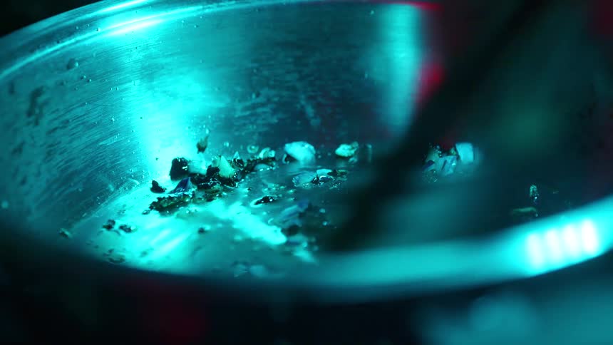 A chef uses tongs to stir and sauté ingredients in a pan under dramatic, stylized blue lighting