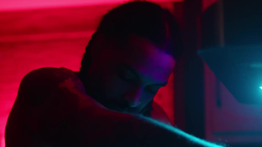 A focused chef works on cooking in a kitchen illuminated by vibrant red and blue neon lights