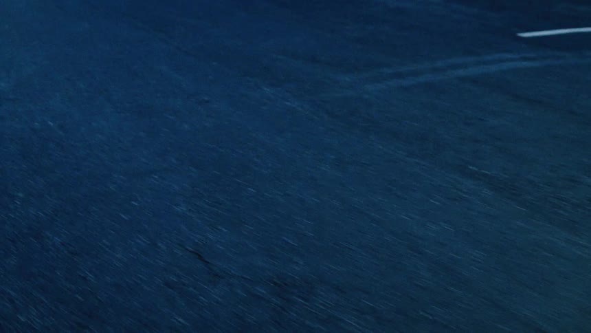 A moody, low-angle point-of-view shot of an asphalt road speeding by at night