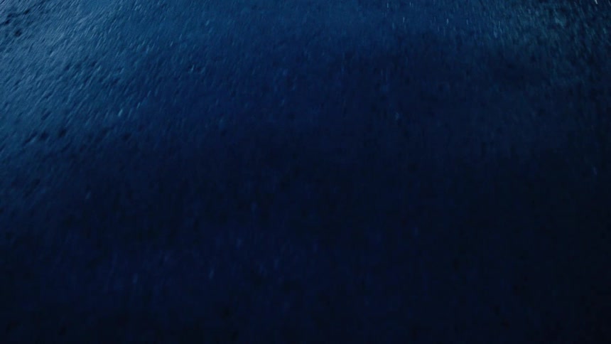 A dramatic, high-angle close-up of heavy rain falling on a wet street at night, illuminated by a cool blue light