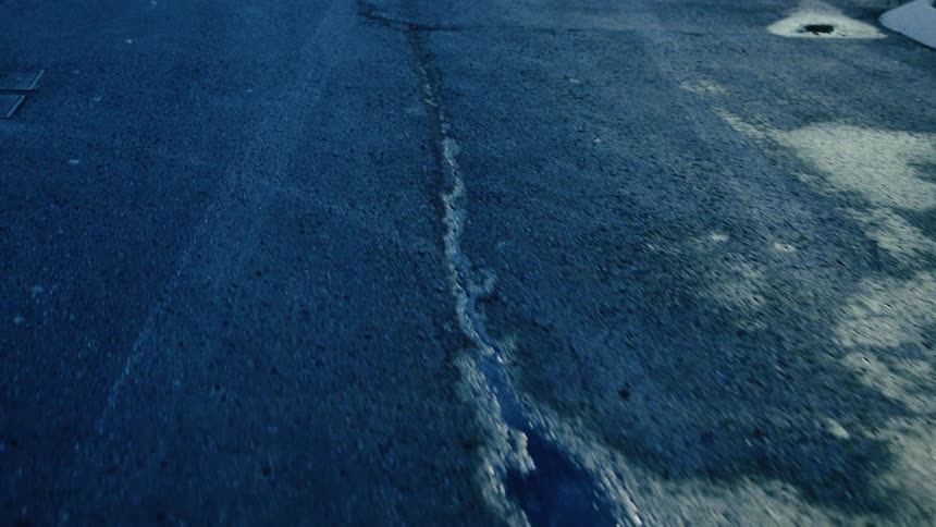 The mysterious shadow of a person is cast upon dark, wet pavement, creating a moody, film noir atmosphere