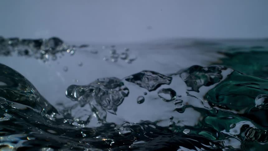 Dramatic super slow-motion shot of a stream of clear water pouring and creating turbulent waves and bubbles