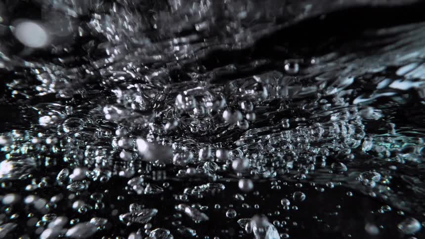 An abstract macro shot of turbulent water and rising air bubbles in slow motion against a black background