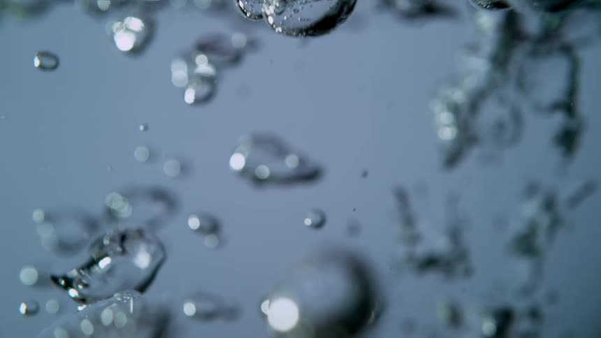 Extreme close-up in slow motion of water pouring and creating shimmering bubbles that float beneath the surface
