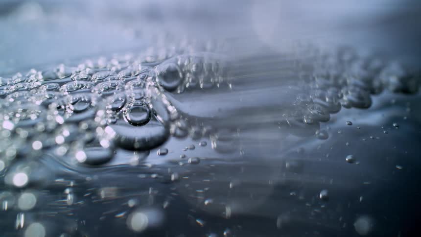 Abstract macro shot of bubbles and ripples on a dark, reflective water surface in slow motion