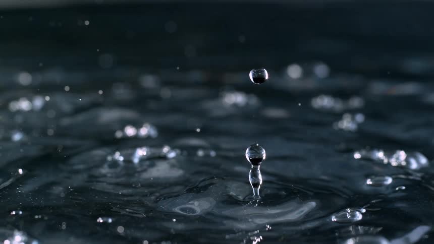 A mesmerizing slow-motion close-up of a single water droplet falling and rebounding off a still surface against a dark background