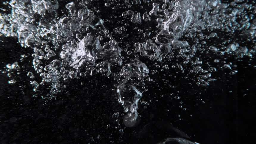 Slow motion of a torrent of air bubbles rising through clear water against a black background