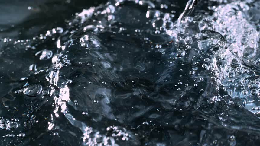 Mesmerizing close-up of water bubbling and rippling across a dark surface in super slow motion