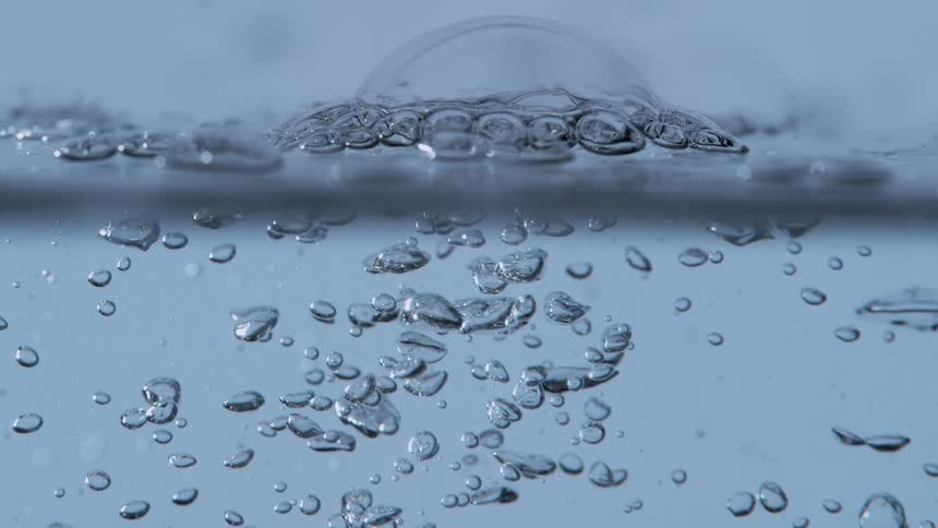 Slow-motion macro shot of air bubbles floating up through clear water and popping on the surface