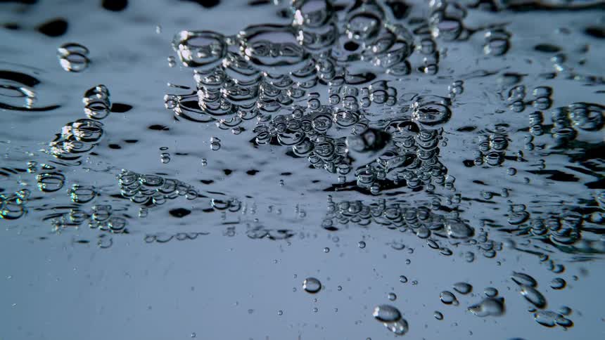 Slow motion underwater view of air bubbles floating on the shimmering surface of clear blue water
