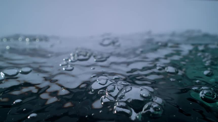Macro slow motion shot of water being filled, creating ripples and bubbles on the surface