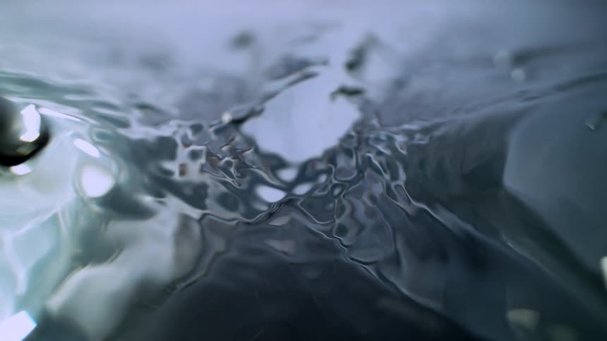 Slow motion, close-up shot of dark, moody water rippling and creating abstract patterns