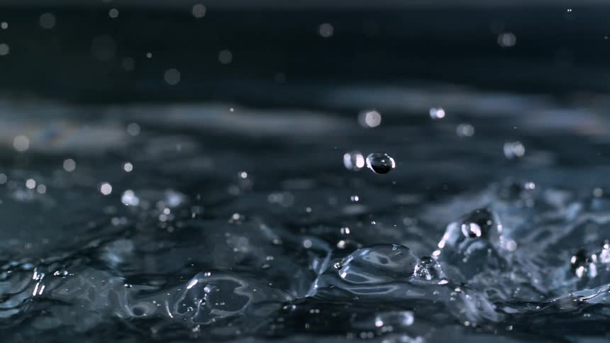A stream of clear water falls into a dark pool, creating intricate splashes and droplets in extreme slow motion