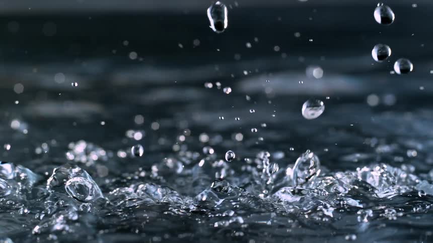 A super slow-motion closeup of countless raindrops falling into dark water, creating a mesmerizing display of splashes and ripples