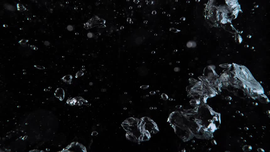 Mesmerizing slow-motion close-up of clear air bubbles floating upwards through water against a stark black background