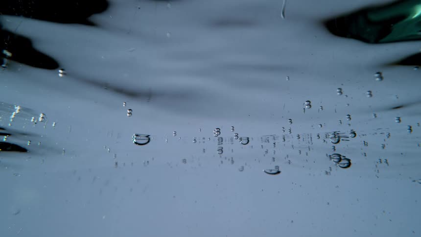 A serene underwater view shows gentle ripples and tiny bubbles floating just beneath the surface in slow motion