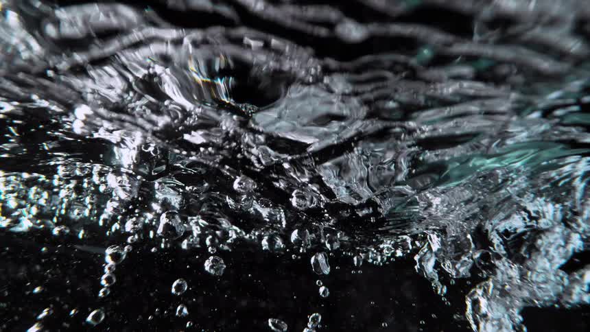 An underwater view of clear water bubbling in super slow motion against a black background