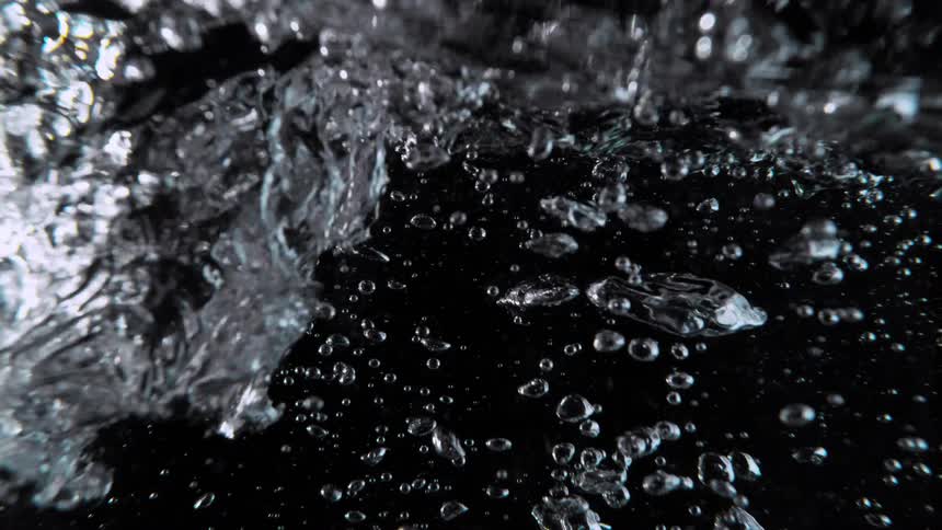 An abstract, super slow-motion view of turbulent water with countless air bubbles rising against a black background