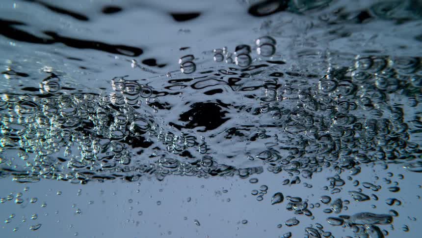 An abstract underwater view of turbulent water with air bubbles rising to the surface in slow motion