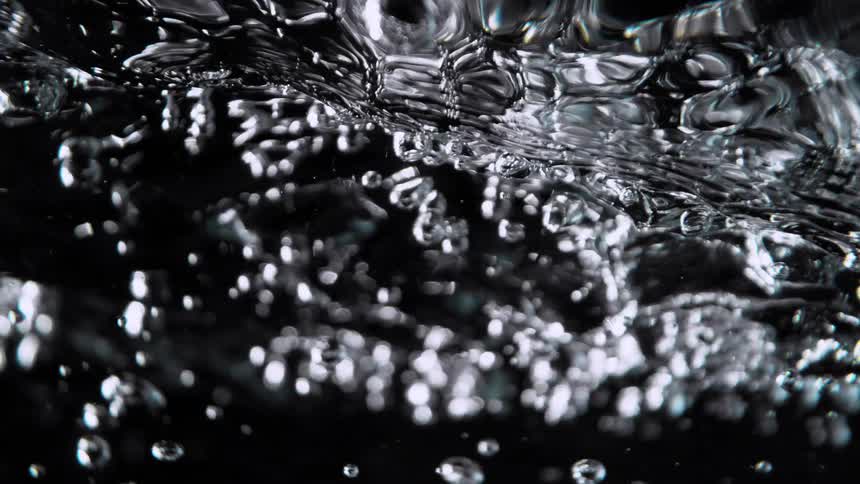 An extreme close-up of turbulent water with bubbles rising in super slow motion against a dark background