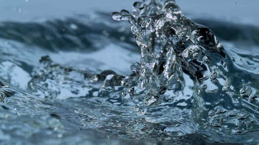 A super slow motion close-up of crystal clear water being poured, creating beautiful splashes, bubbles, and ripples on the surface