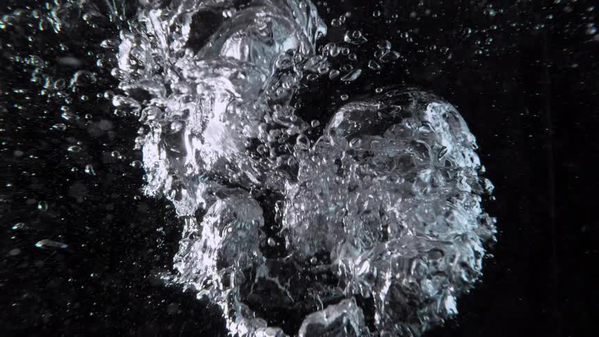 An underwater view of chaotic air bubbles rising to the surface in slow motion against a dark background