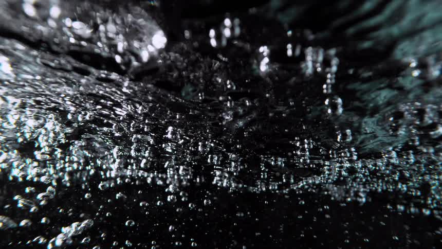 Extreme slow-motion close up of turbulent water and air bubbles boiling against a black background