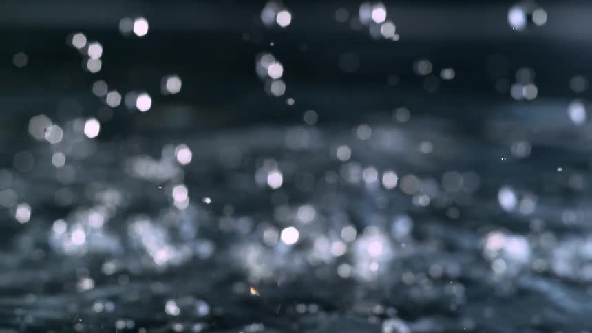 A beautiful abstract shot of out-of-focus water droplets falling in super slow motion, creating a sparkling bokeh effect on the surface