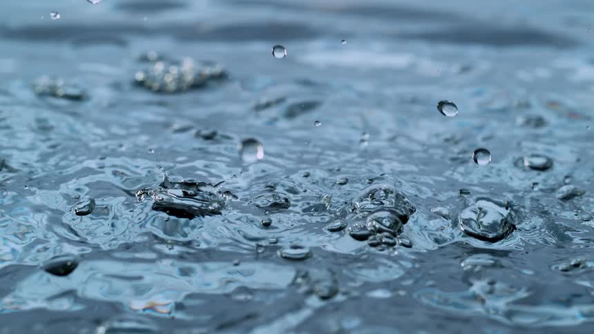 A mesmerizing super slow motion macro shot captures water droplets falling and creating intricate splashes and ripples on a clear blue surface