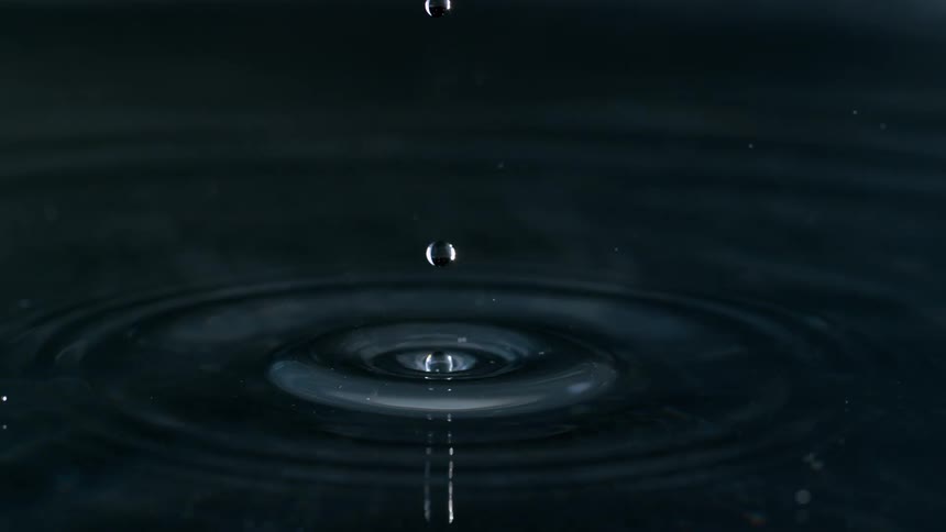 A stunning super slow-motion close-up of a single water droplet hitting a dark surface and creating concentric ripples