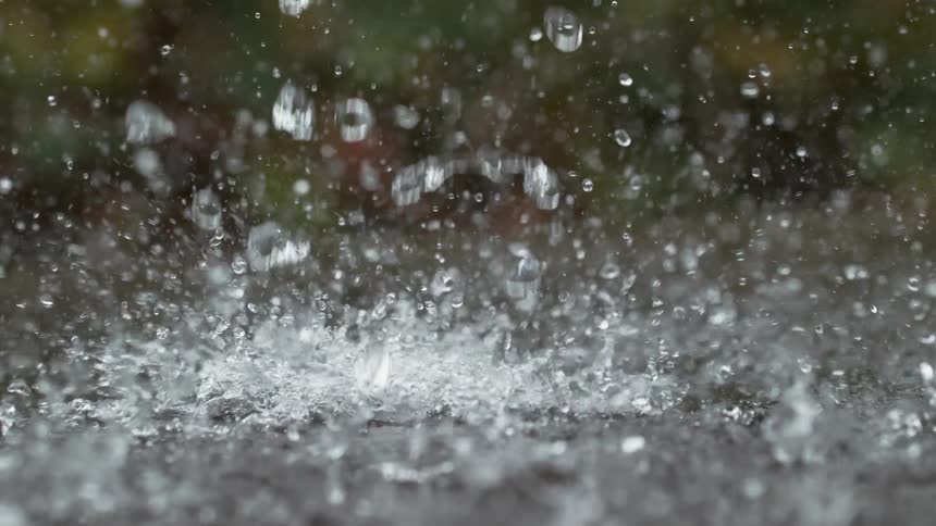 Heavy raindrops splash onto the pavement in a dramatic super slow-motion close-up