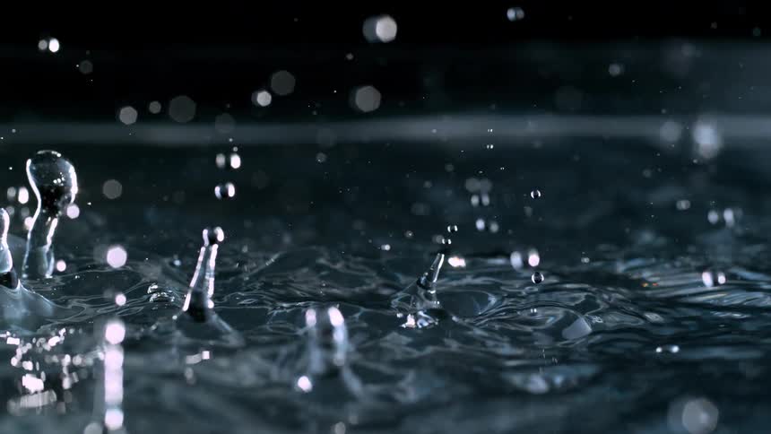 Mesmerizing super slow motion close-up of water droplets splashing and creating ripples against a dark background