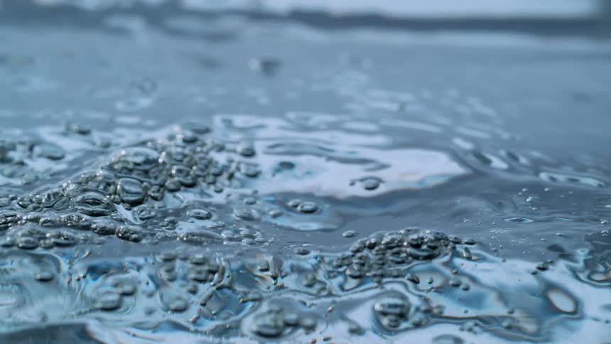 Mesmerizing slow motion close up of a clear blue water surface rippling and forming bubbles before a large splash