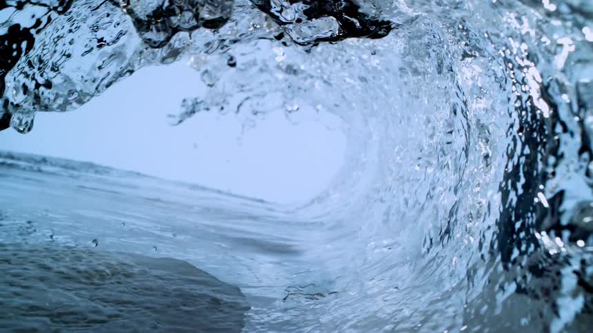 An extreme close-up, super slow-motion view from inside a perfect blue wave as it curls and crashes over the camera