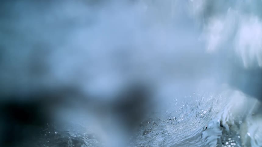 An abstract, close-up view of a clear water wave cresting in super slow motion