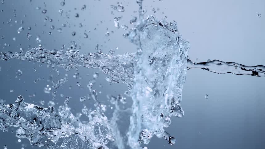 A jet of clean water splashes and flows horizontally across the screen against a grey background in super slow motion
