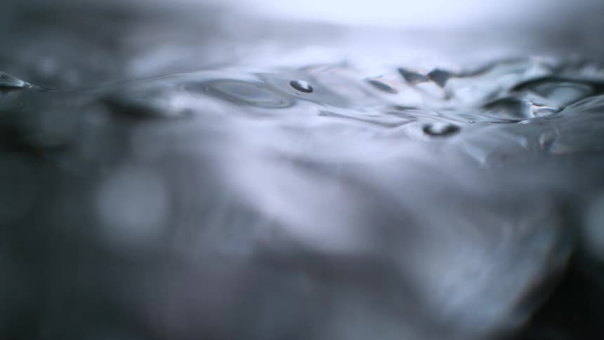 A dramatic super slow-motion macro shot captures water bubbling and splashing before the camera submerges into the turbulent liquid
