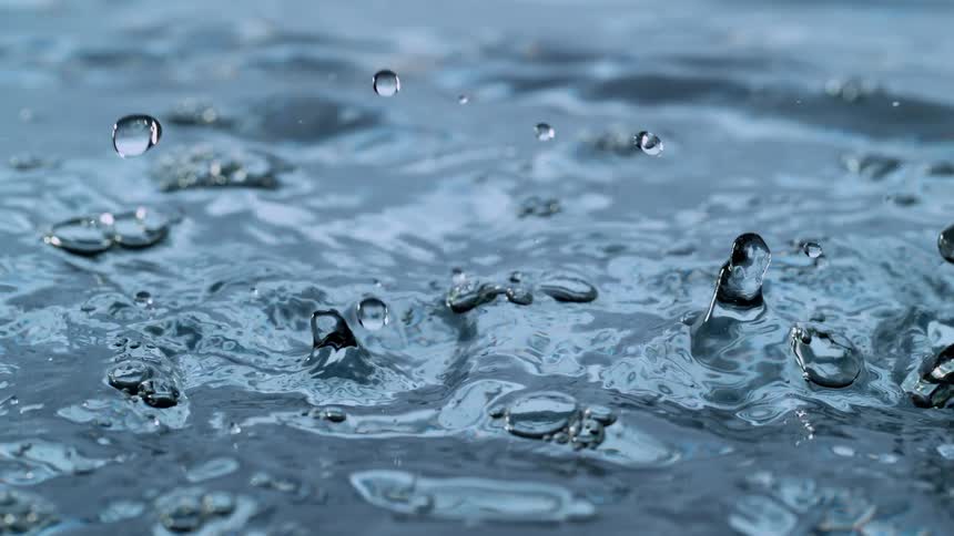 An extreme close-up of water droplets falling into a body of water in super slow motion, creating splashes and bubbles