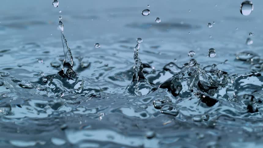 A super slow motion closeup shot captures water droplets falling into a clear body of water, creating beautiful ripples and splashes