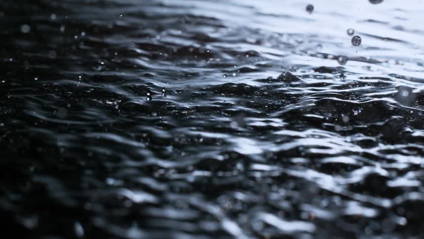 Raindrops fall in mesmerizing super slow-motion onto a dark, rippling water surface