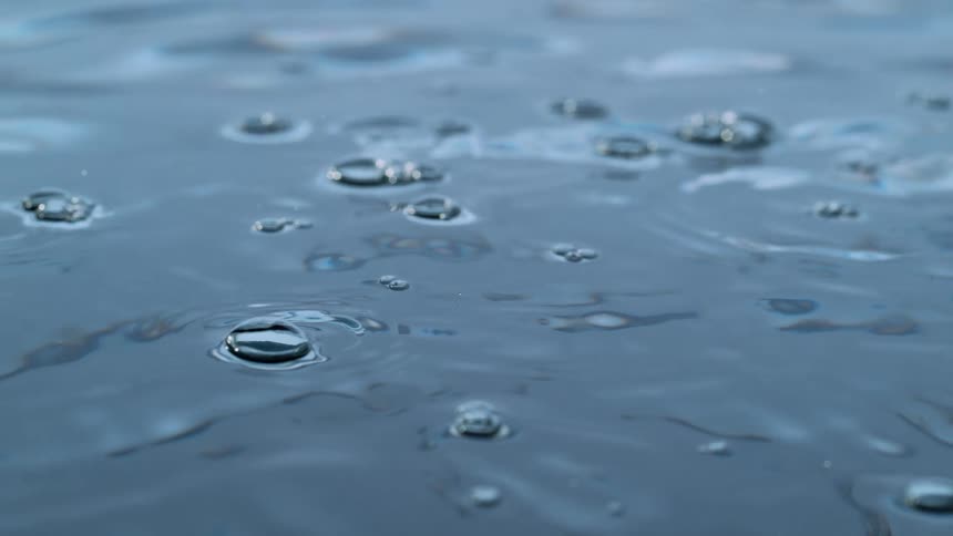 Super slow-motion macro shot of calm, dark blue water with bubbles gently popping and creating soft ripples